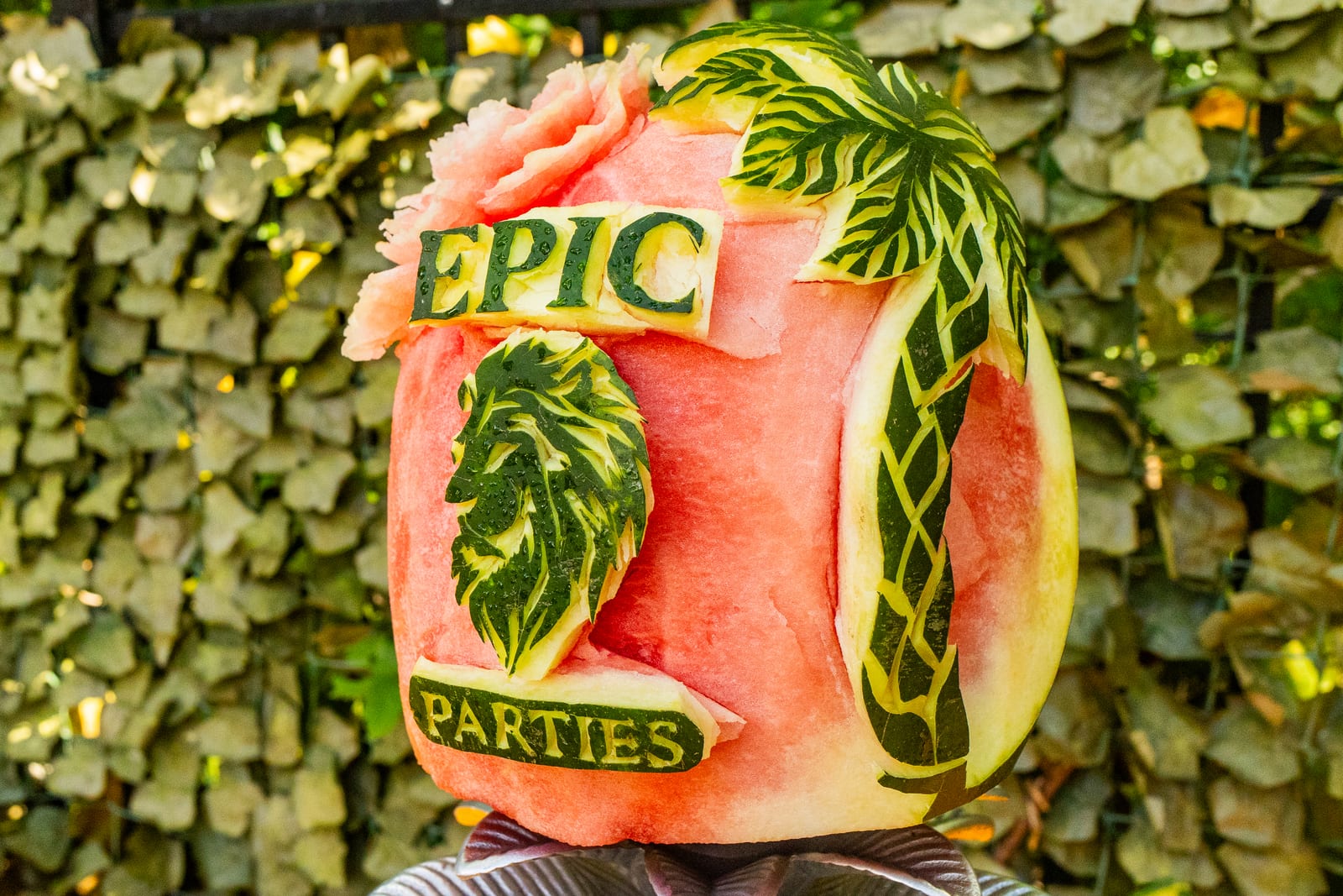 Watermelon carved with the EPIC PARTIES name and palm trees against a foliage wall