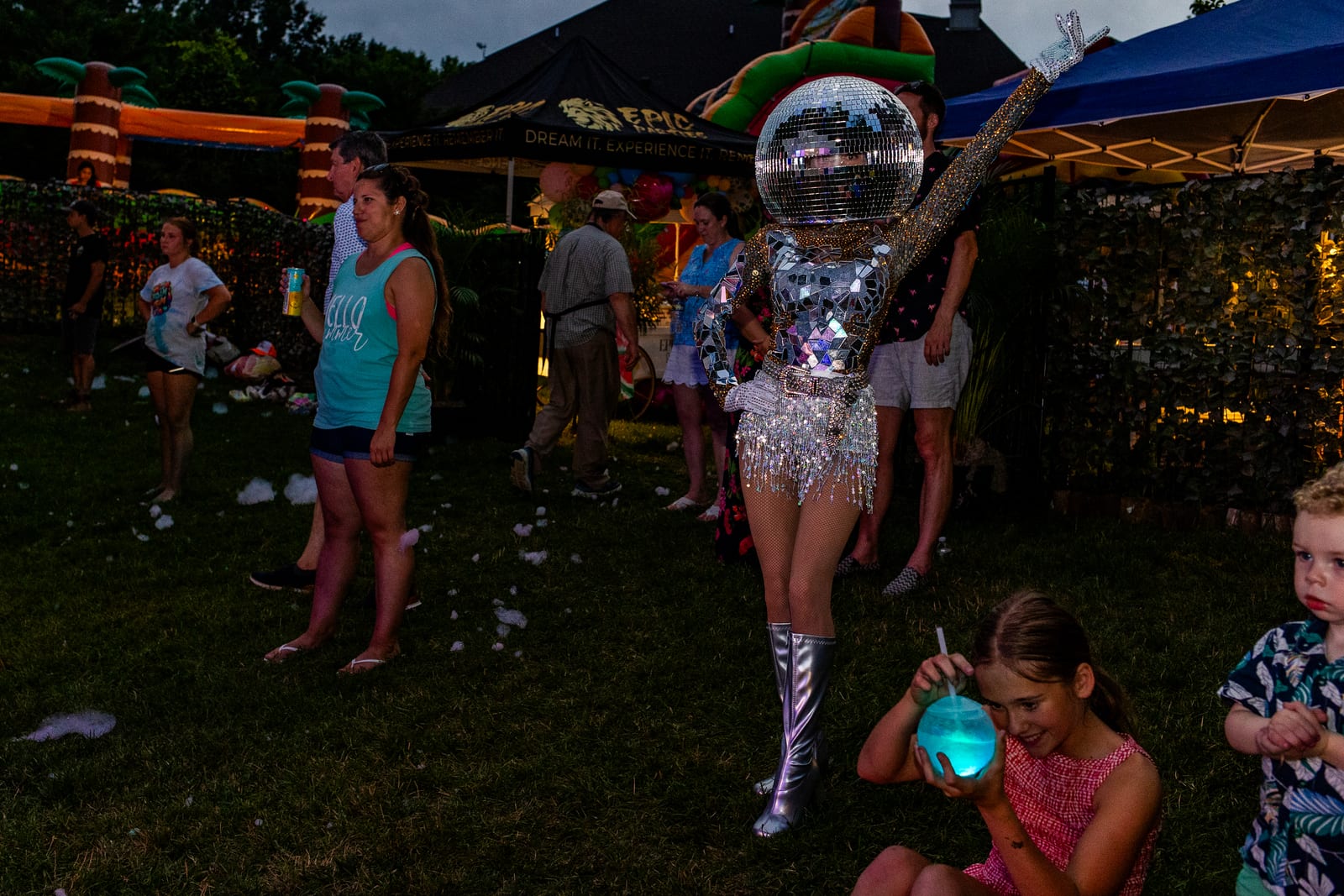Mirror-ball costumed performer among guests on a lawn in the evening
