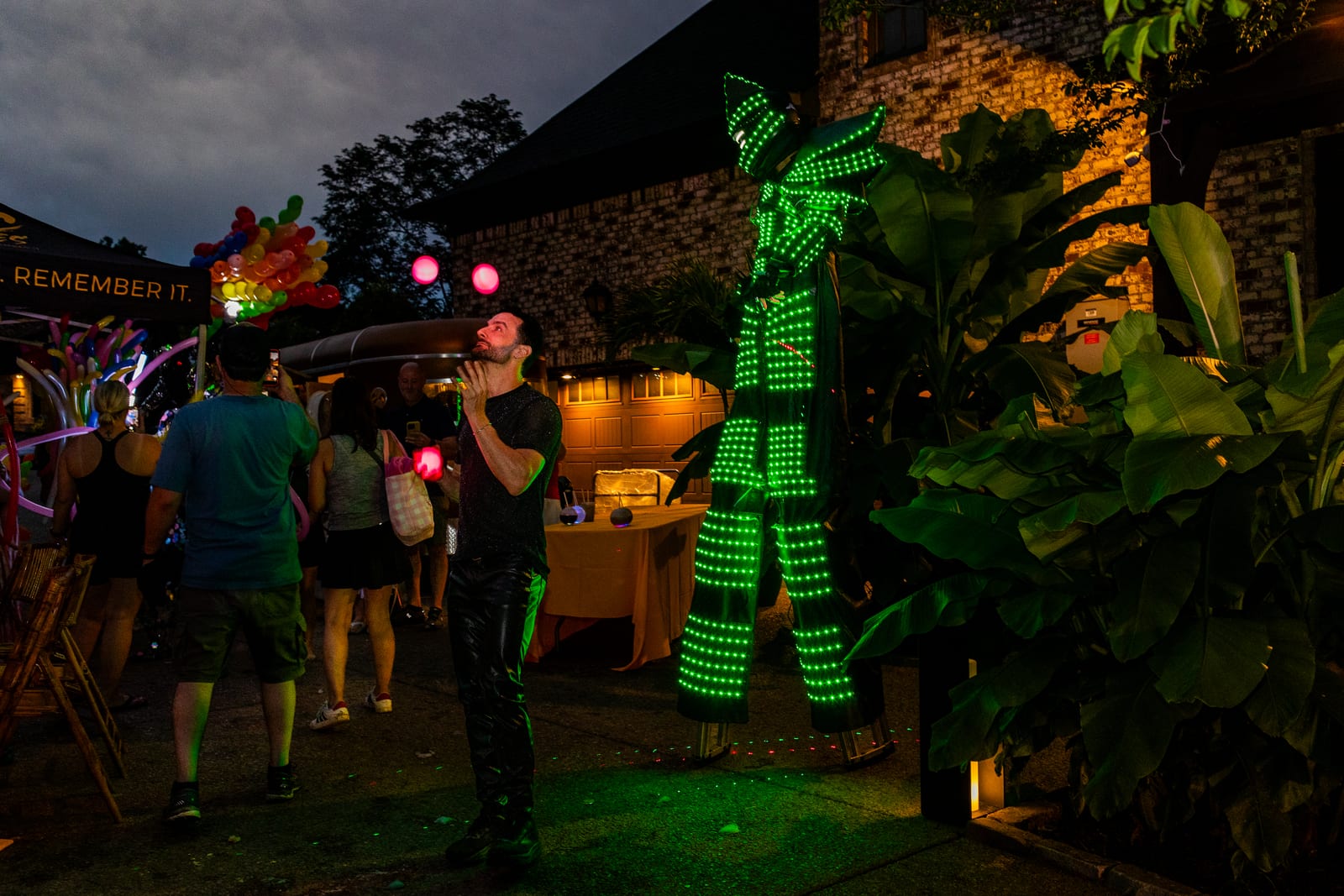 Performer in a glowing green LED suit standing among guests at night