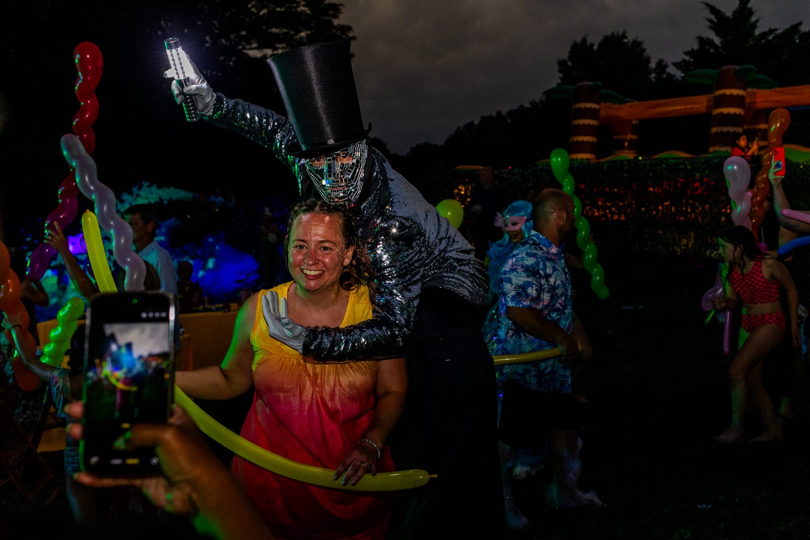 Top-hatted performer in a mirrored suit towering over guests holding glowing wands