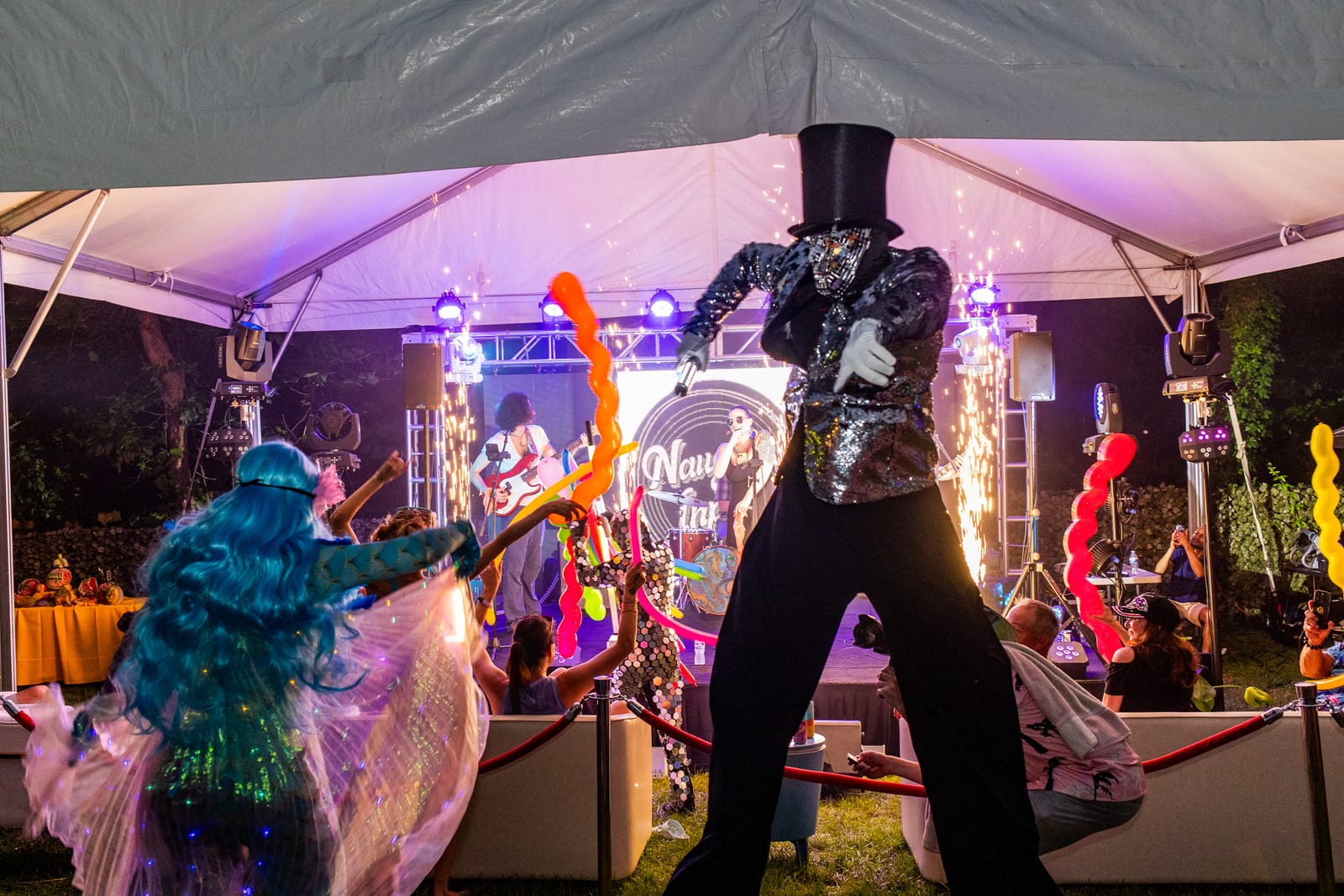 Stilt walker and costumed performers on a marquee stage as spark fountains fire