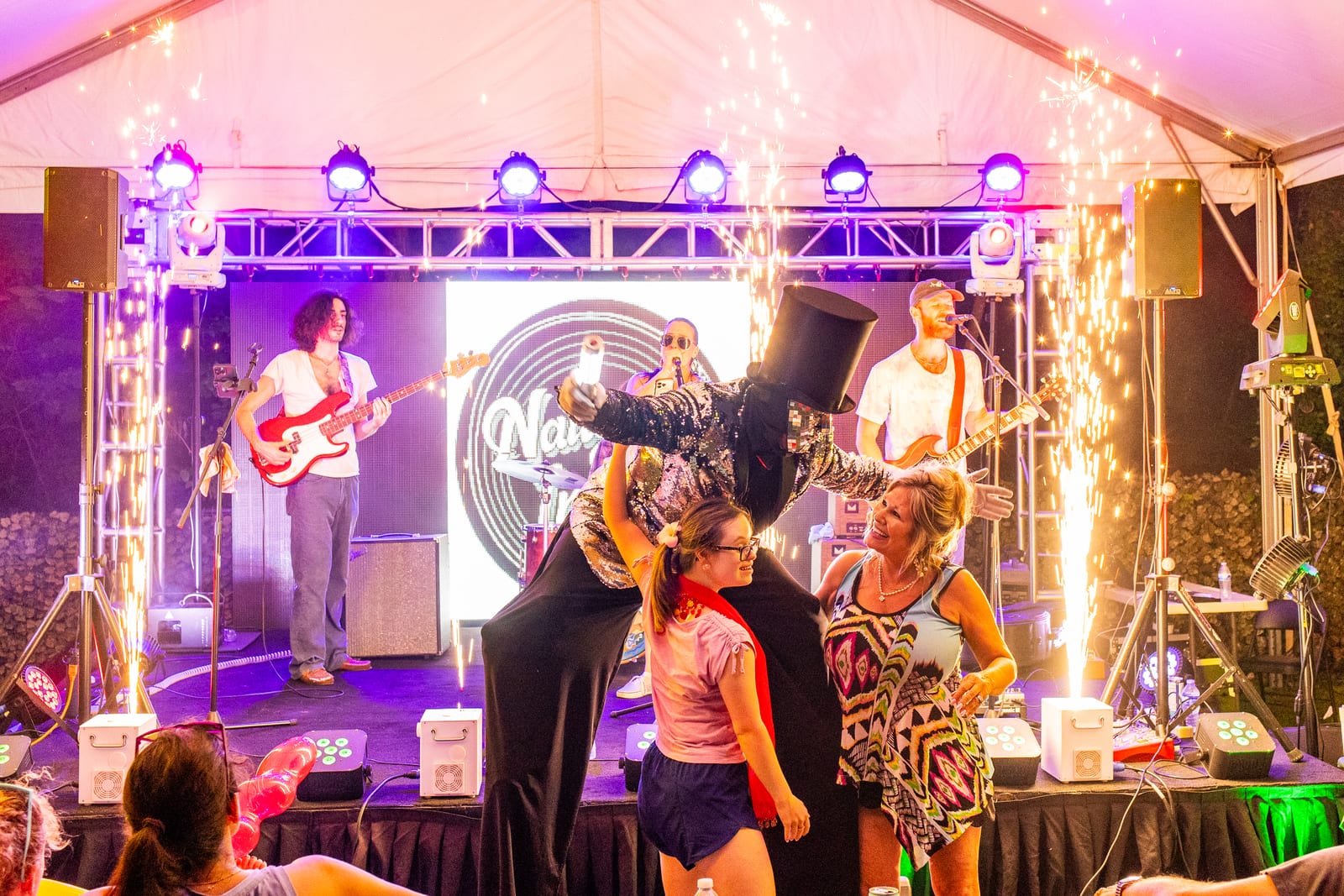 Live band on a lit stage firing spark fountains while guests dance in front