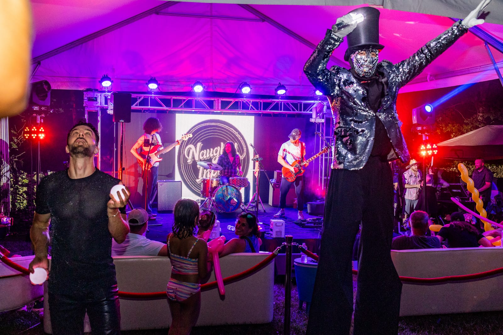 Mirrored stilt walker raising an arm above a seated crowd in front of a band