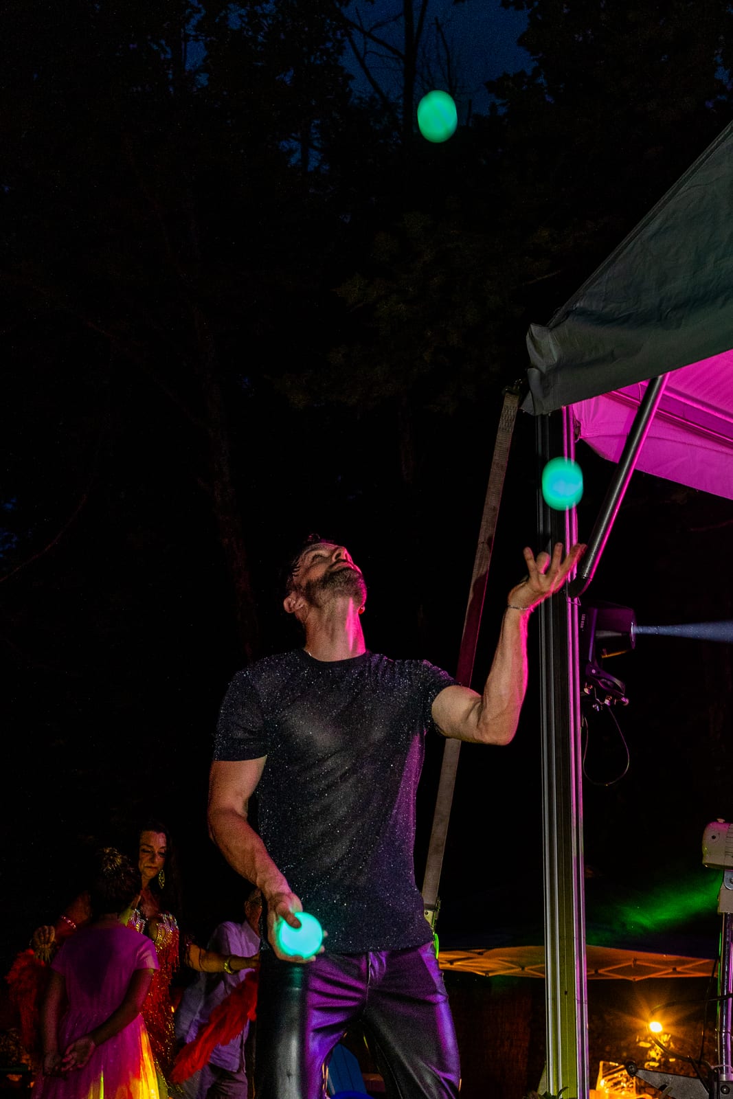 Juggler working three glowing balls under a canopy at night