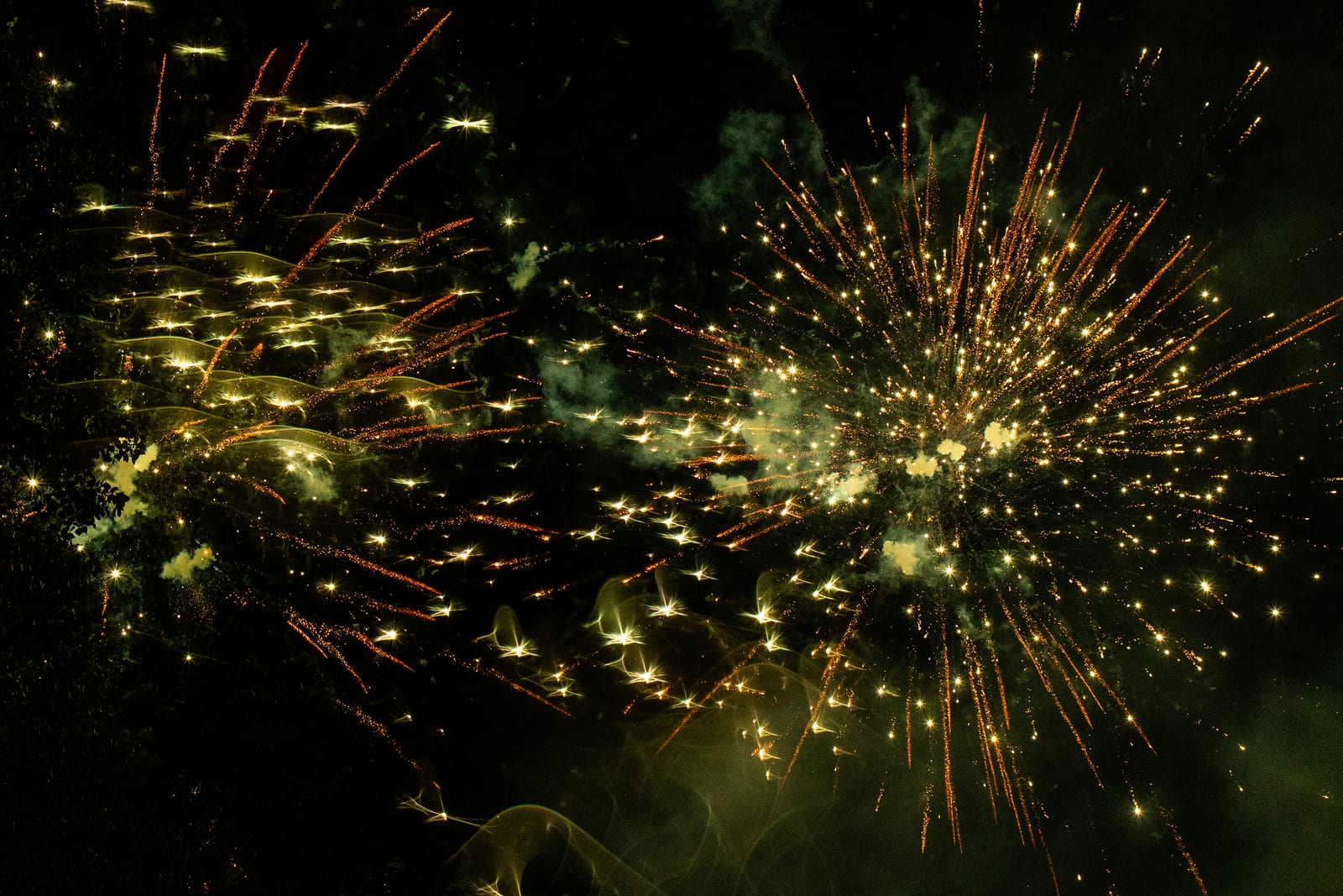 Golden fireworks bursting above the lights of a party below
