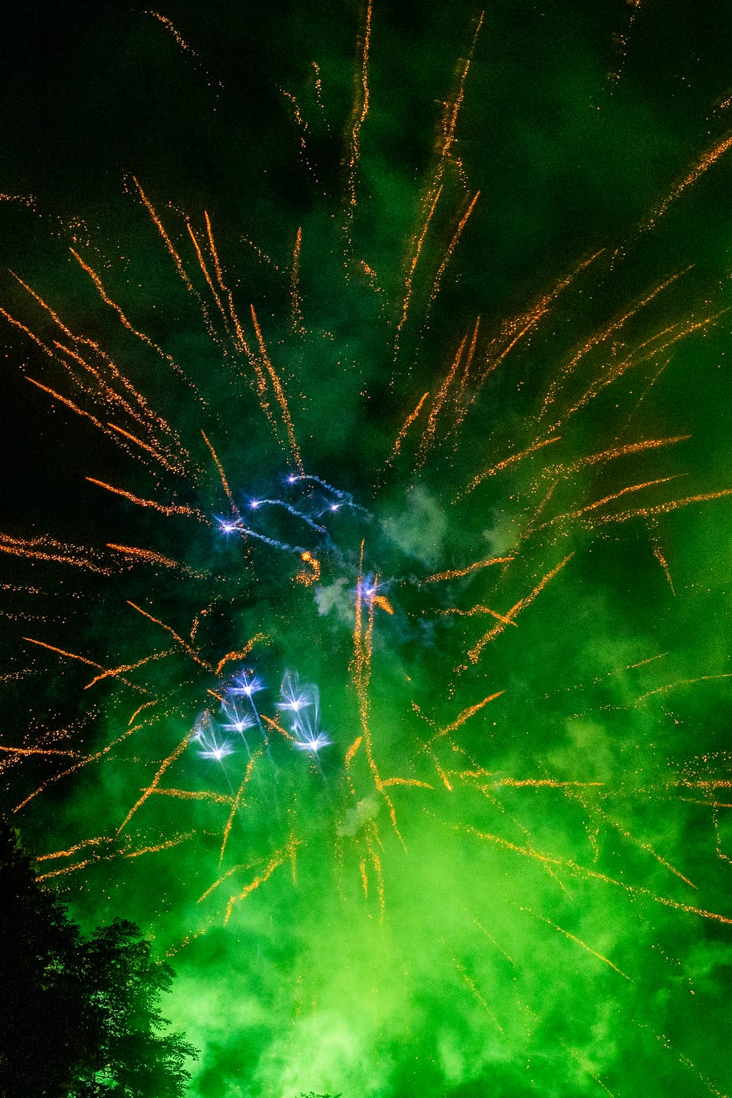 Firework bursting through billowing green smoke against a night sky