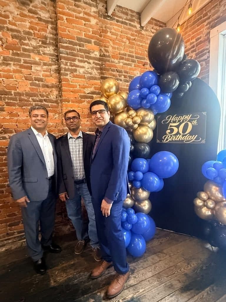 Guests beside a navy, black and gold balloon arch reading Happy 50th Birthday on exposed brick