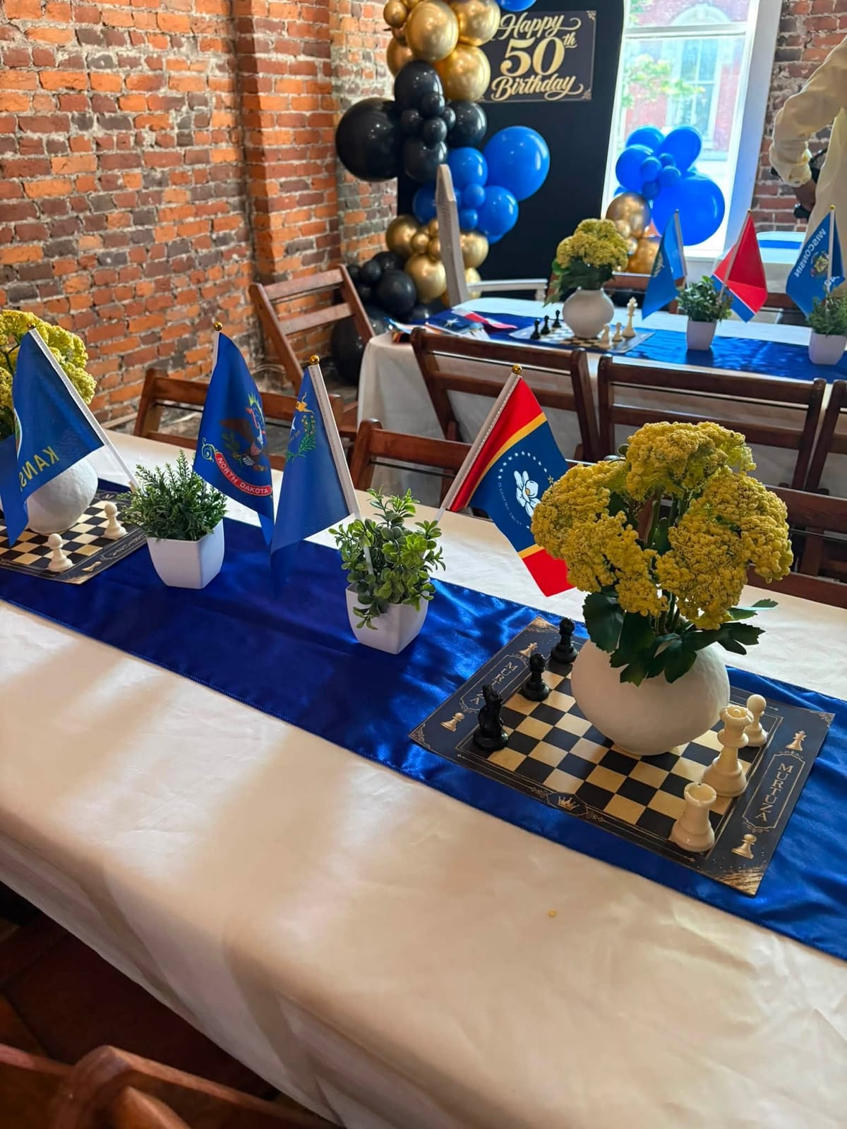 Navy, gold and black 50th birthday setup with chessboard runners and floral centrepieces in a brick venue