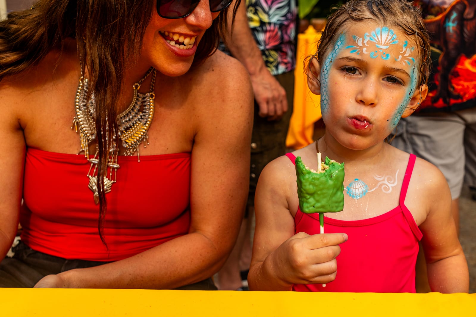 An adult and a face-painted child laughing together over a frozen treat