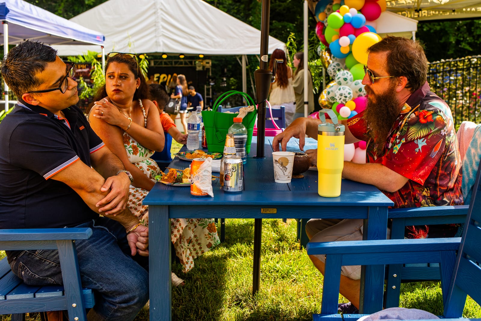 Guests seated with drinks at a picnic table beneath a canopy at a garden party
