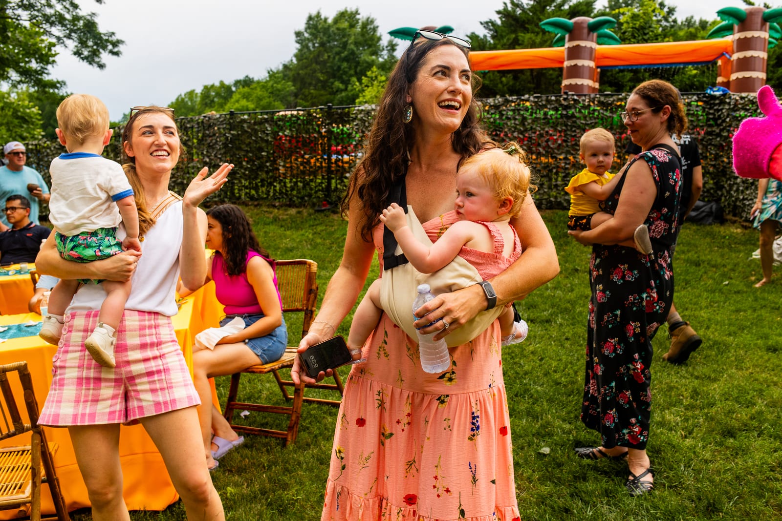 Guests holding babies at a garden party with an inflatable slide behind them