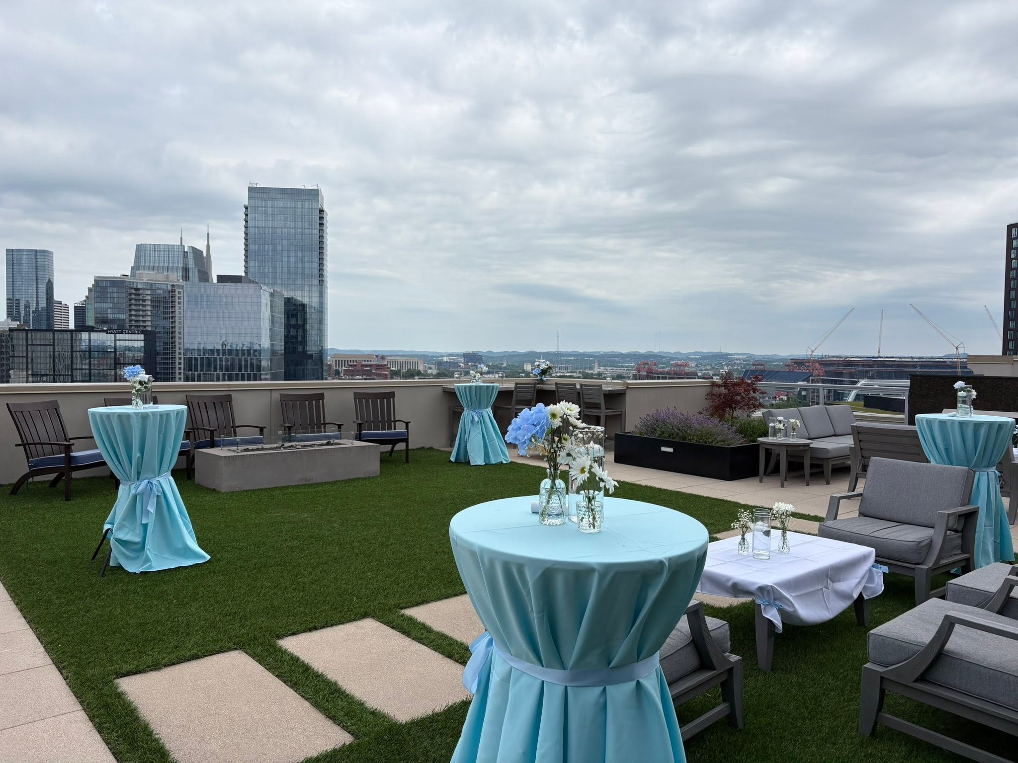 Rooftop terrace set with pale blue linen cocktail tables, white and blue florals and a fire pit, overlooking the Nashville skyline