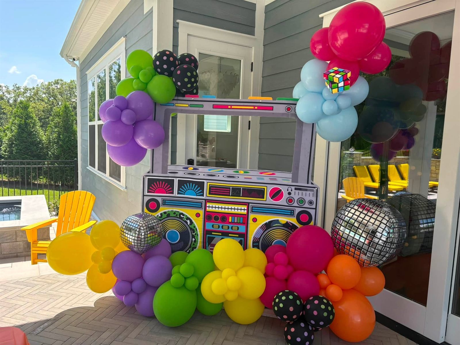A giant boom-box photo booth frame surrounded by a balloon garland in pink, purple, green, yellow and orange with disco ball balloons