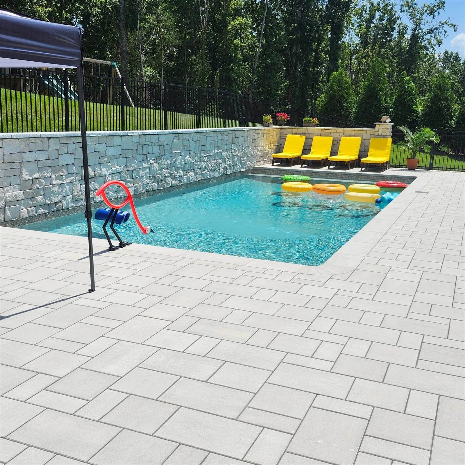 A backyard pool lined with bright yellow loungers and floating rings in green, yellow, orange and red
