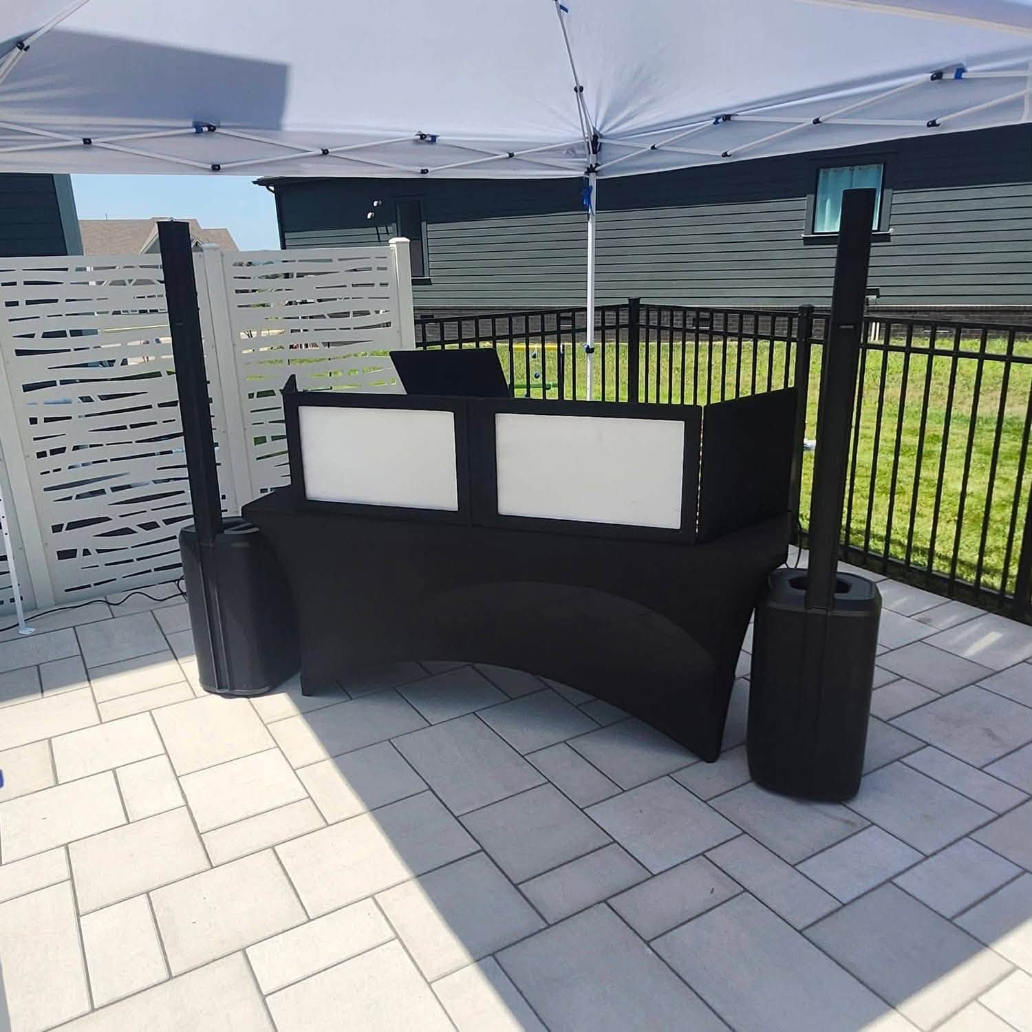 A DJ booth with white light panels and column speakers set up under a canopy on a pool deck