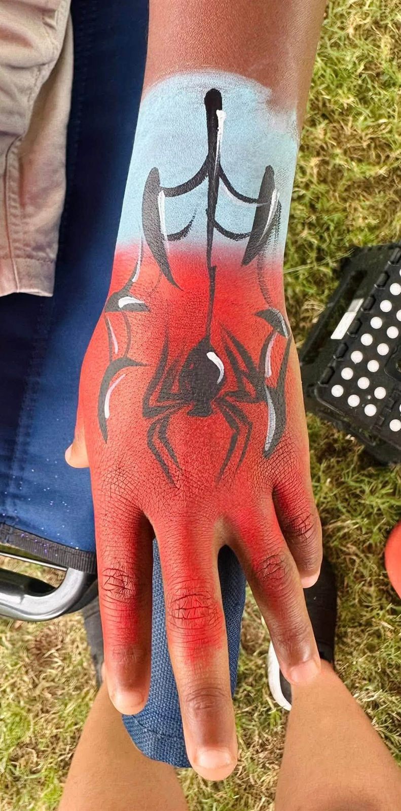 A child's hand and wrist painted with a red and blue spider web design