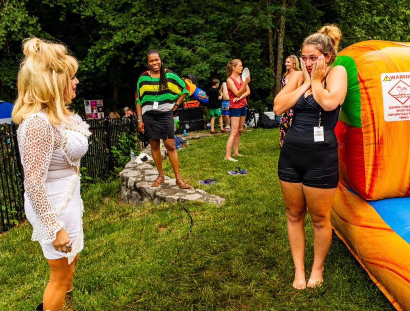 A Dolly Parton tribute artist in a white fringe dress surprising a party guest who has both hands pressed to her face